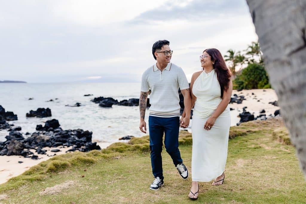 William and Roshni walking along the water holding hands and smiling