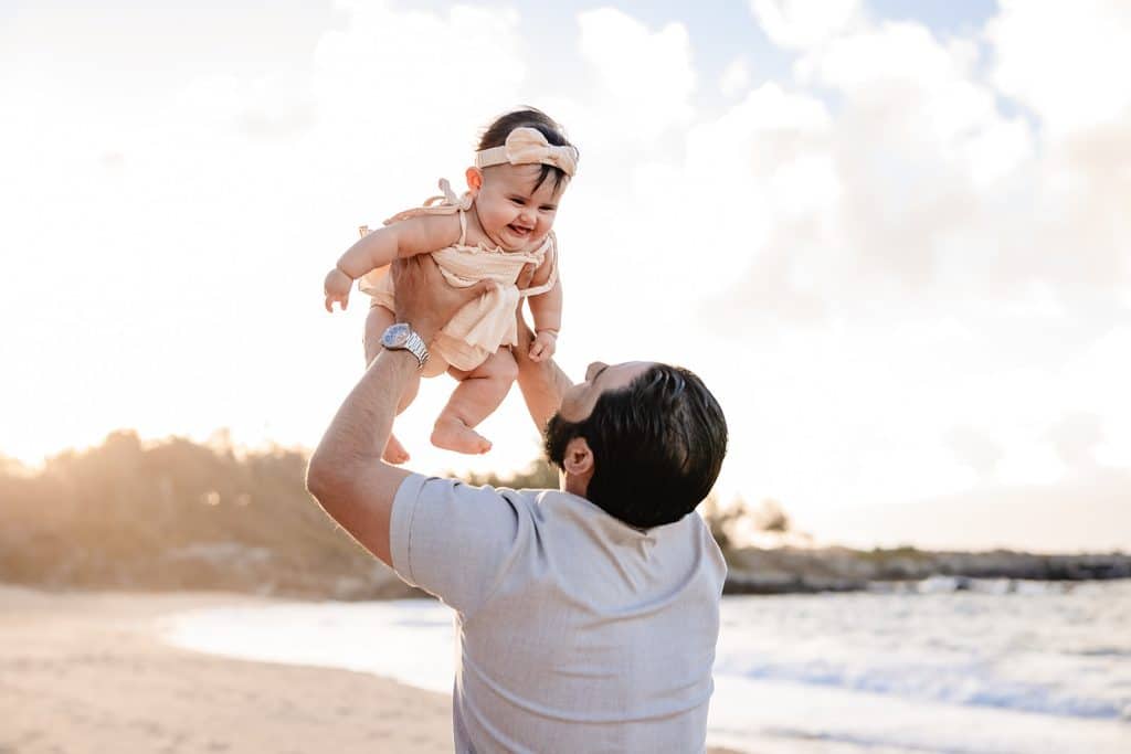 Andy throwing his baby girl into the air while the sun sets behind them on the beach.