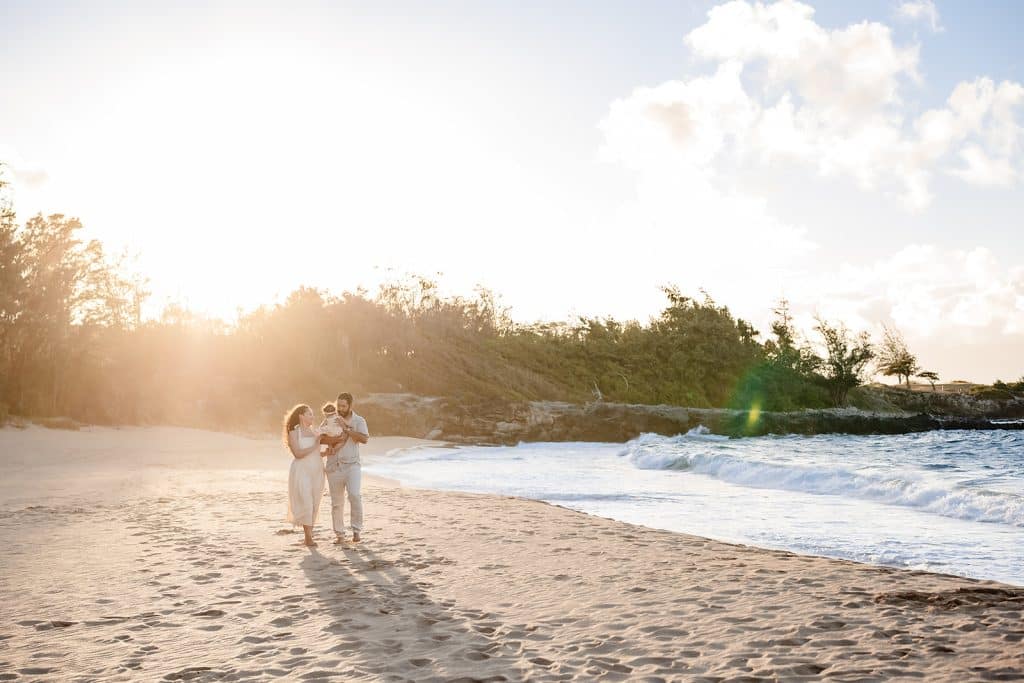 Andy and Tanya talking to their baby girl as they walk the shoreline at sunset.