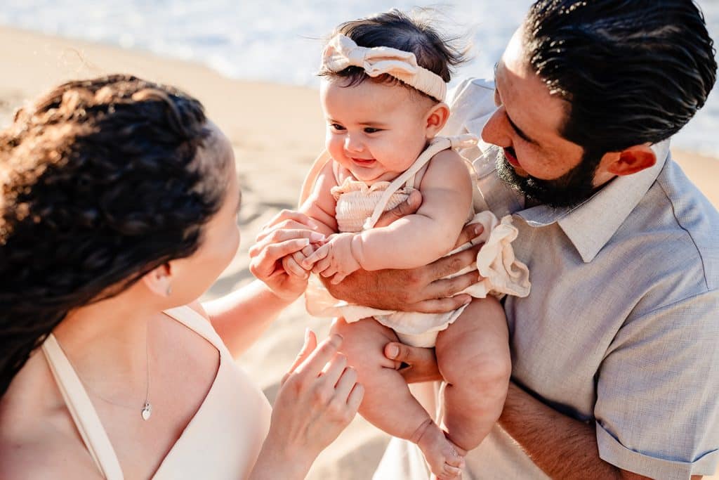 A close up of Tanya playing with her babies hads as the baby smiles at her, and Andy is holding the baby and smiling at her.