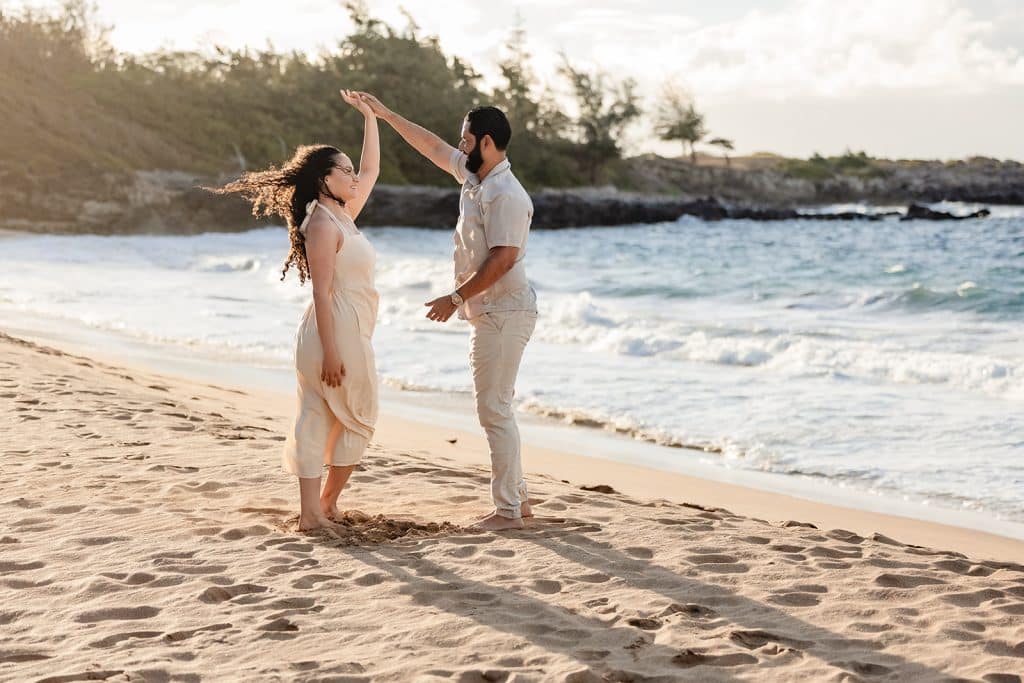 Andy twirling Tanya around in the sand while the waves crash behind them as the sun sets.