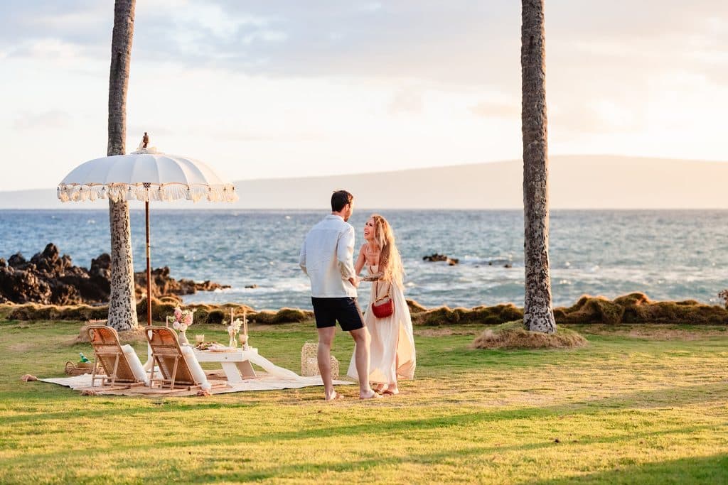 Patrick and Rachel holding hands while standing next to the picnic setup. Rachel is laughing at what Patrick is telling her. 