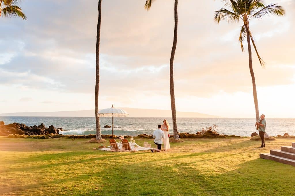 A wide angle photo of Patrick proposing to Rachel. A musician is to their right playing guitar and singing softly. 