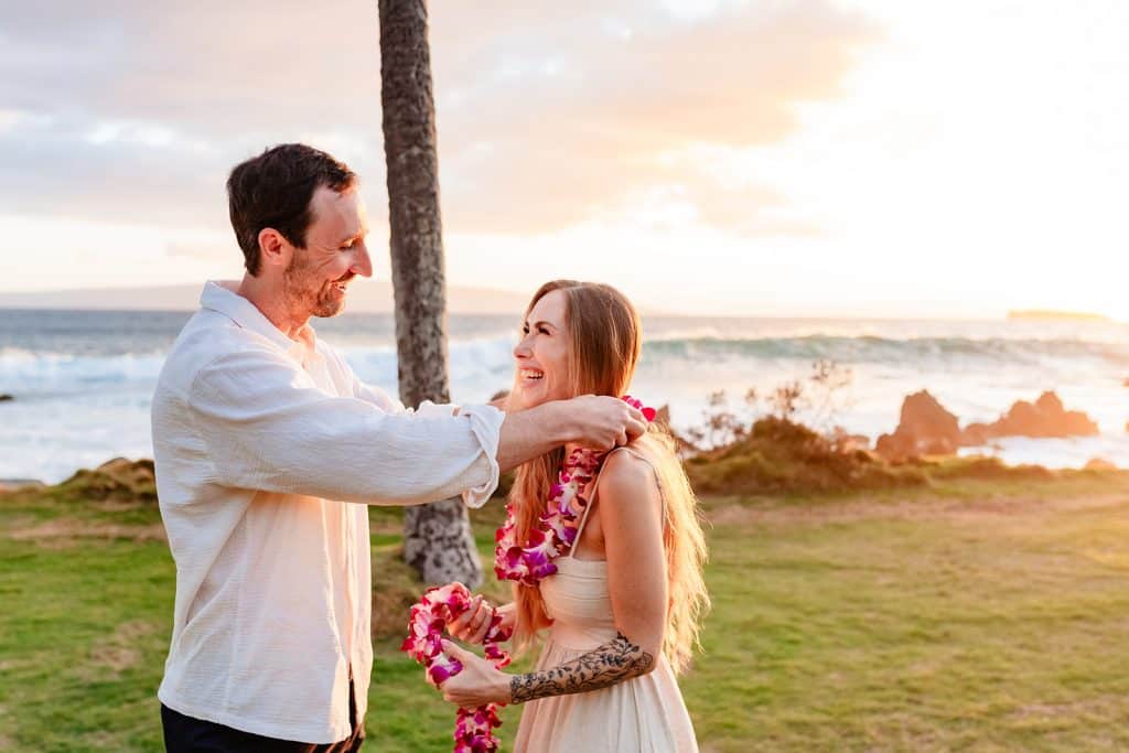 Patrick and Rachel smiling at each other while Patrick drapes a lei over Rachel's neck.