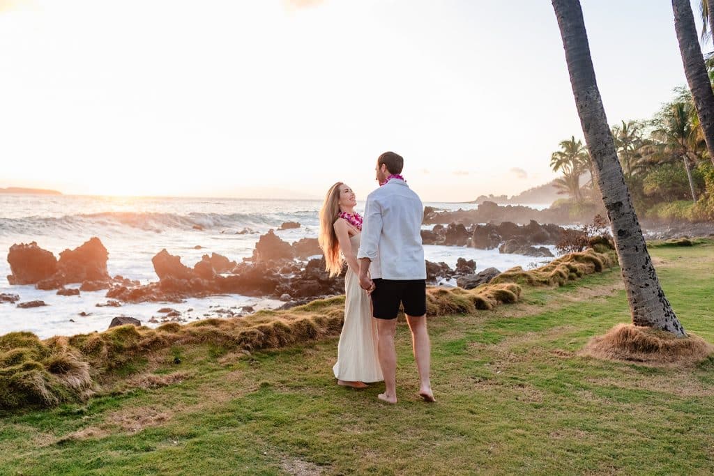 Patrick and Rachel holding hands and leaning into each other with the ocean and sunset behind them.