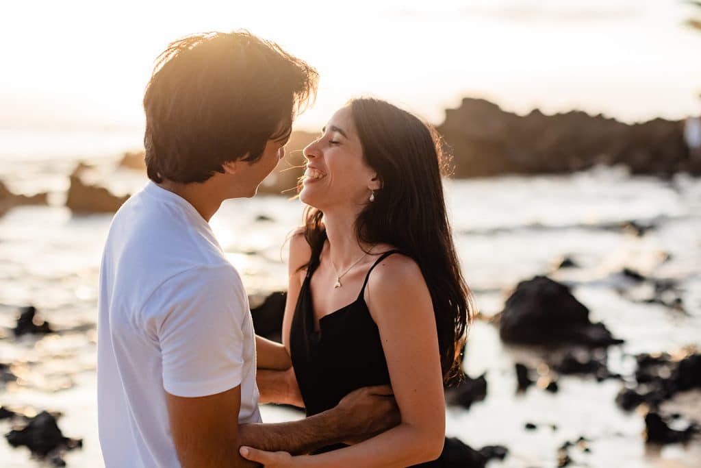 Alejandra laughing at Hector as they embrace with the sun setting behind them