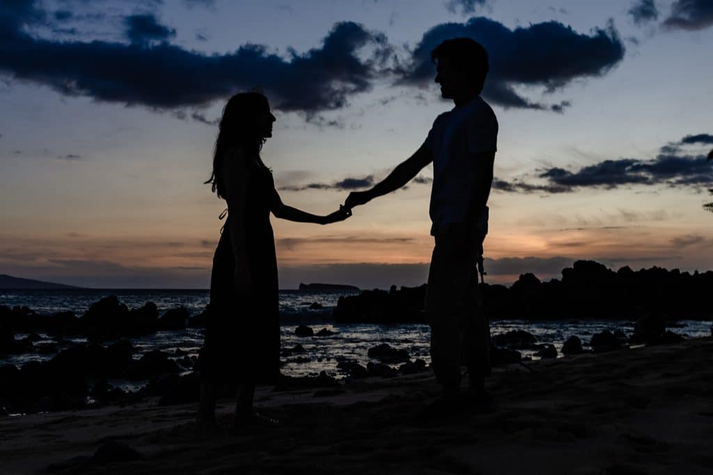Alejandra and Hector's silohouttes holding outstretched hands as the sun has set behind them. 