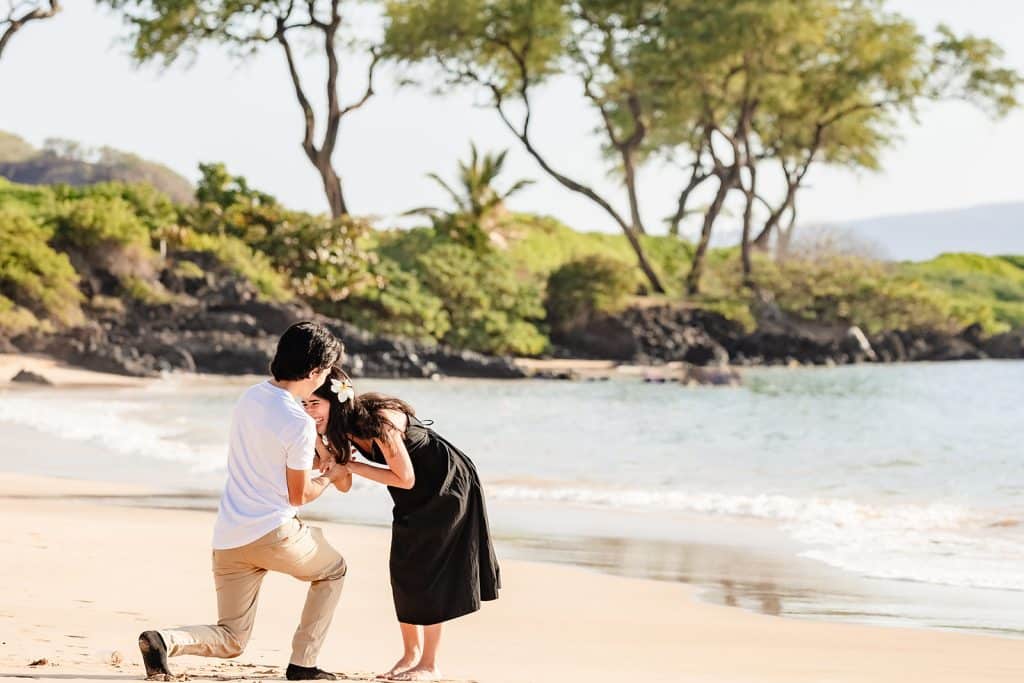 Alejandra leaning down and laughing as Hector is putting on the ring while still down on one knee.