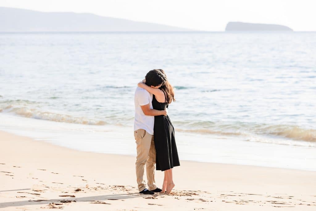 Hector and Alejandra hugging in the sand with the ocean behind them after the proposal is over.