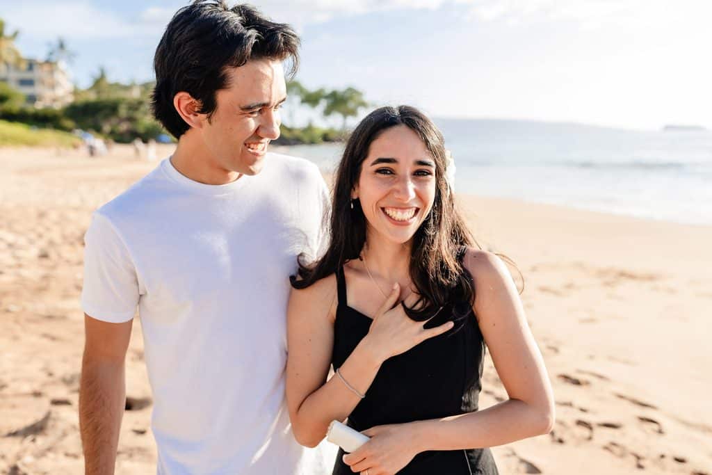 Hector smiling at Alejandra while she smiles and holds her chest looking at the camera.