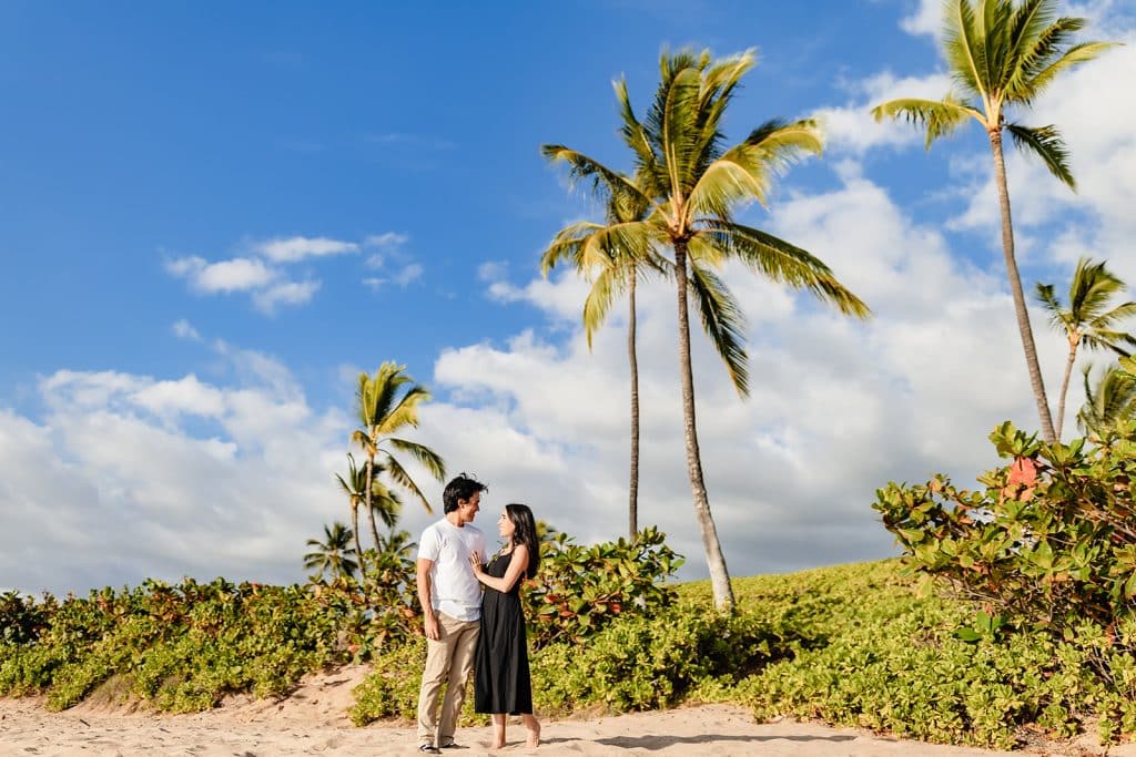 Hector and Alejandra standing side by side and embracing with the palm trees and greenery behind them.