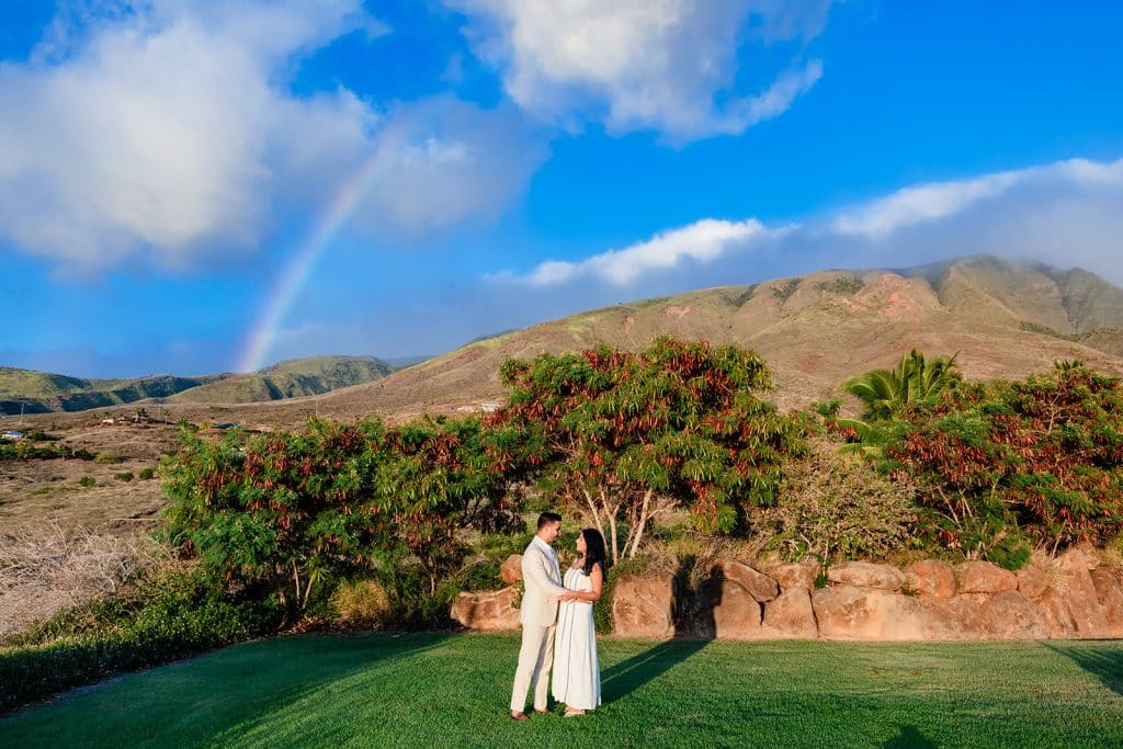 Pruthvi and Tithi embracing with the mountains behind them and a rainbow adorning the sky.