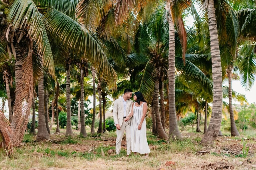 Pruthvi and Tithi smiling and leaning into each other while holding hands. They're standing in front of dozens of palm trees.