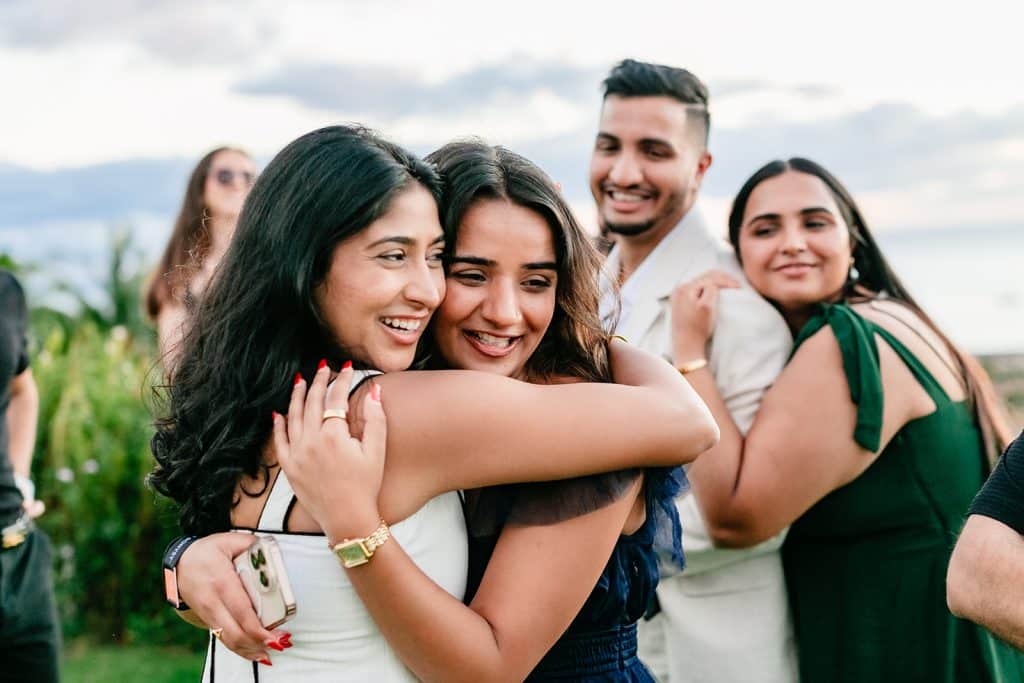 A closeup photo of Tithi hugging one of her family members and smiling. Pruthvi and his sister are in the background out of focus but embracing and smiling at Tithi.