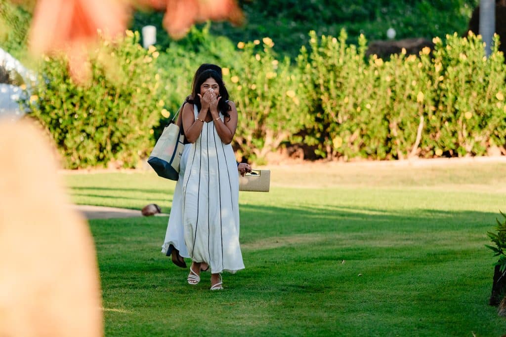 Tithi covering her face with her hands in shock as she sees Pruthvi standing among the flowers.