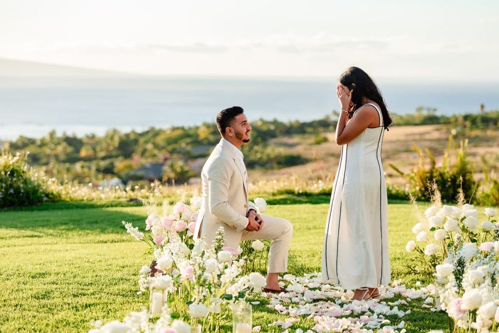A close up photo of Pruthvi on one knee and Tithi holding her hands up to her face in shock.