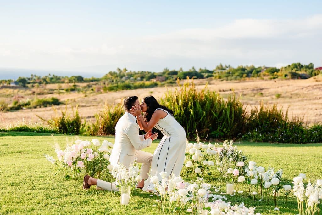 Tithi bending down to give Pruthvi a kiss while he's still on one knee among the florals.