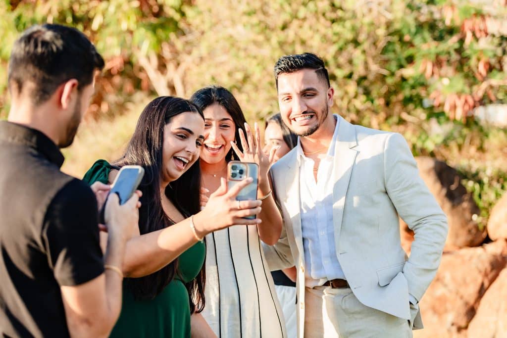 Tithi holding up her hand with her engagement ring to somebody that's on Facetime. Pruthvi is standing next to her smiling as family and friends call and document this moment.