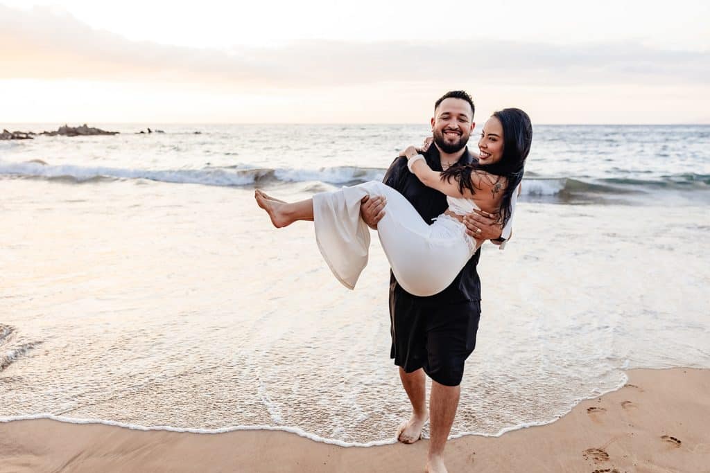 Brandon carrying Alexis towards the camera as they're both smiling and laughing.