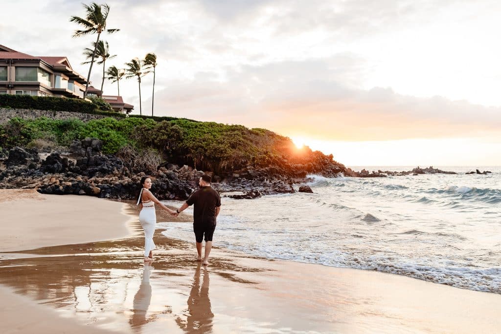 Brandon and Alexis walking towards the water away from the camera. The sun is setting behind the cliffs and Alexis is looking over her shoulder at the camera.