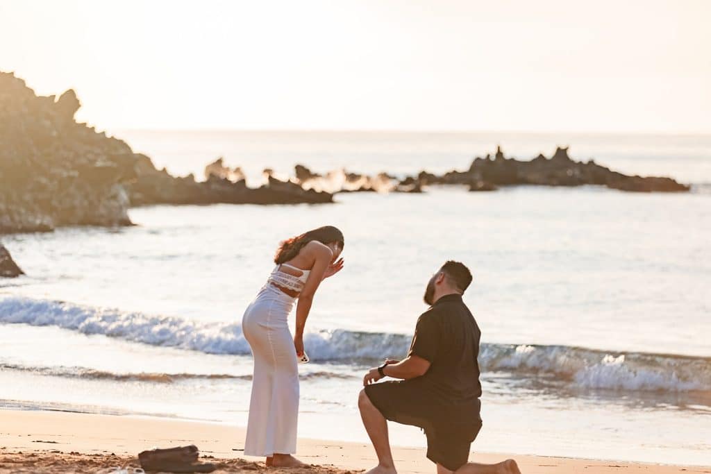 Alexis leaning over and laughing with her hand up to her face while Brandon is down on knee holding the ring.