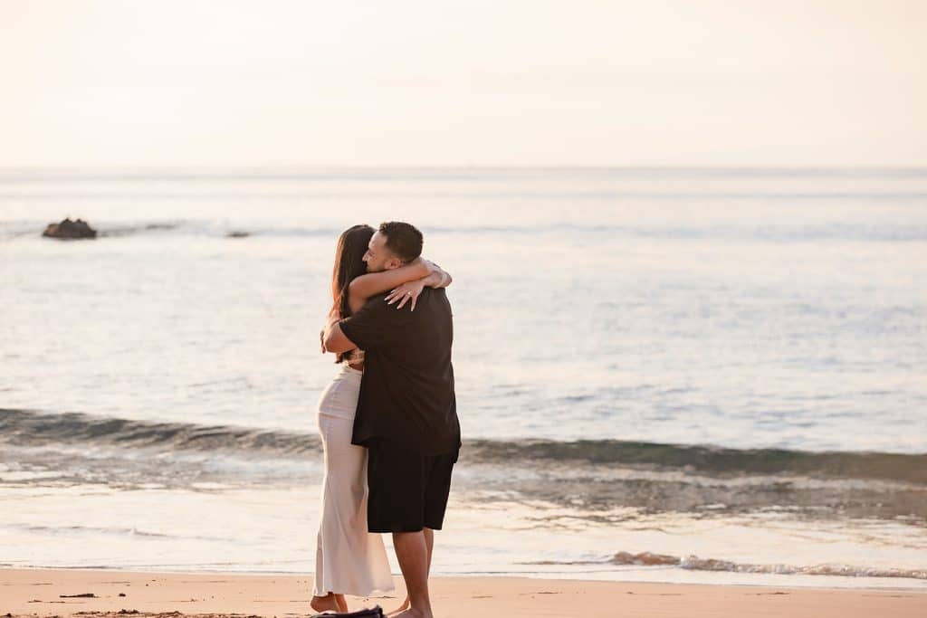 Alexis and Brandon hugging in the sand after his proposal.
