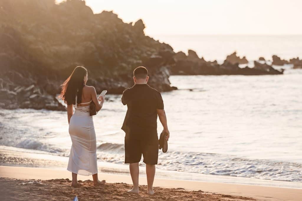 Brandon and Alexis on the shore taking photos of the beach as the sun sets in the horizon. 