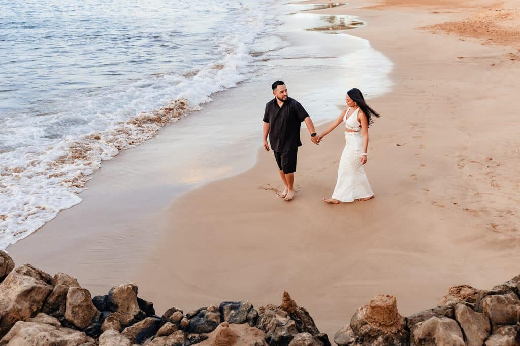 A photo from above of Alexis and Brandon holding hands and walking on the sand towards the water.