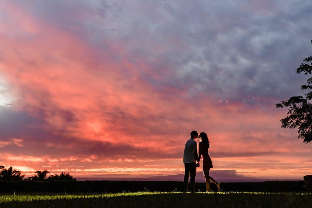 Raynell and Denise sharing a kiss as their silhouette shines against the deep oranges and purples of the sunset.