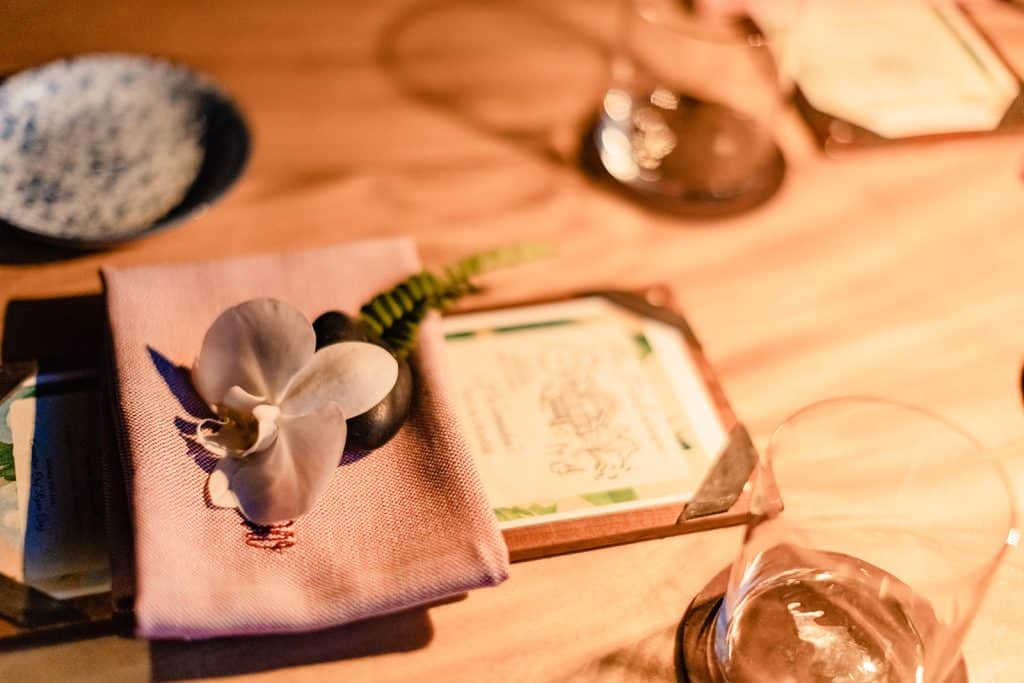 A close up photo of the flower and menu on the table set for two in the treehouse.