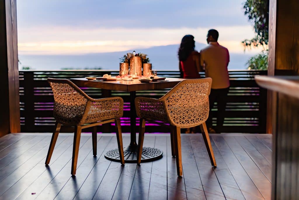The table setting filled with candles and flowers is in the focus of the photo with Raynell and Denise standing against the balcony looking at each other in the background.