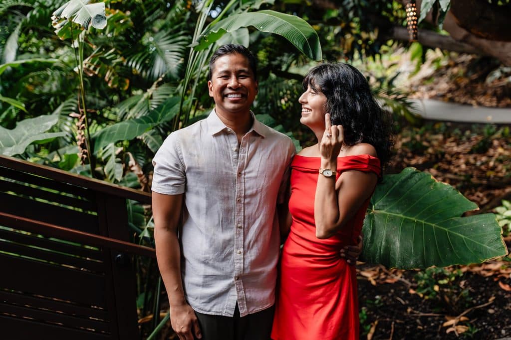 Raynell and Denise standing side by side. Raynell is smiling at the camera while Denise is smiling at Raynell and holding up her ring finger to show off her new engagement ring.