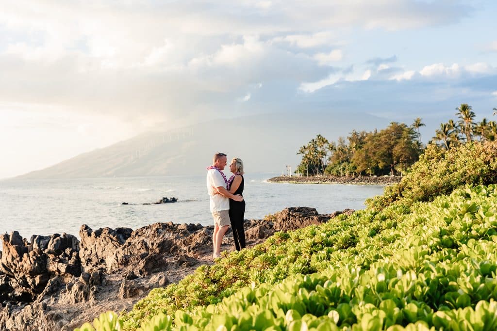 Joy and Andy standing on the cliffside and embracing as the ocean is behind them.