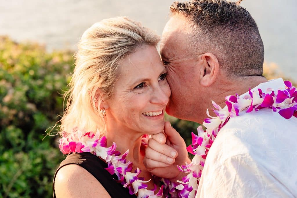 A close up photo of Andy holding Joy's chin and whispering in her ear as she smiles.