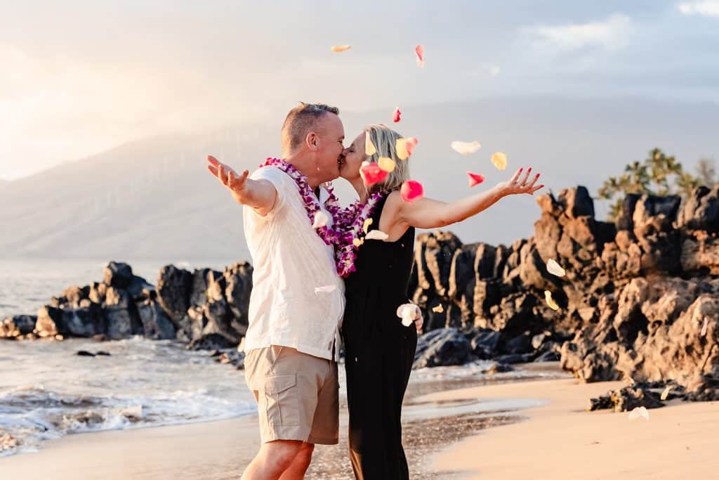 Andy and Joy sharing a kiss after throwing flower petals into the air. Flower petals scattered in front of them while they're arms are still outstretched.