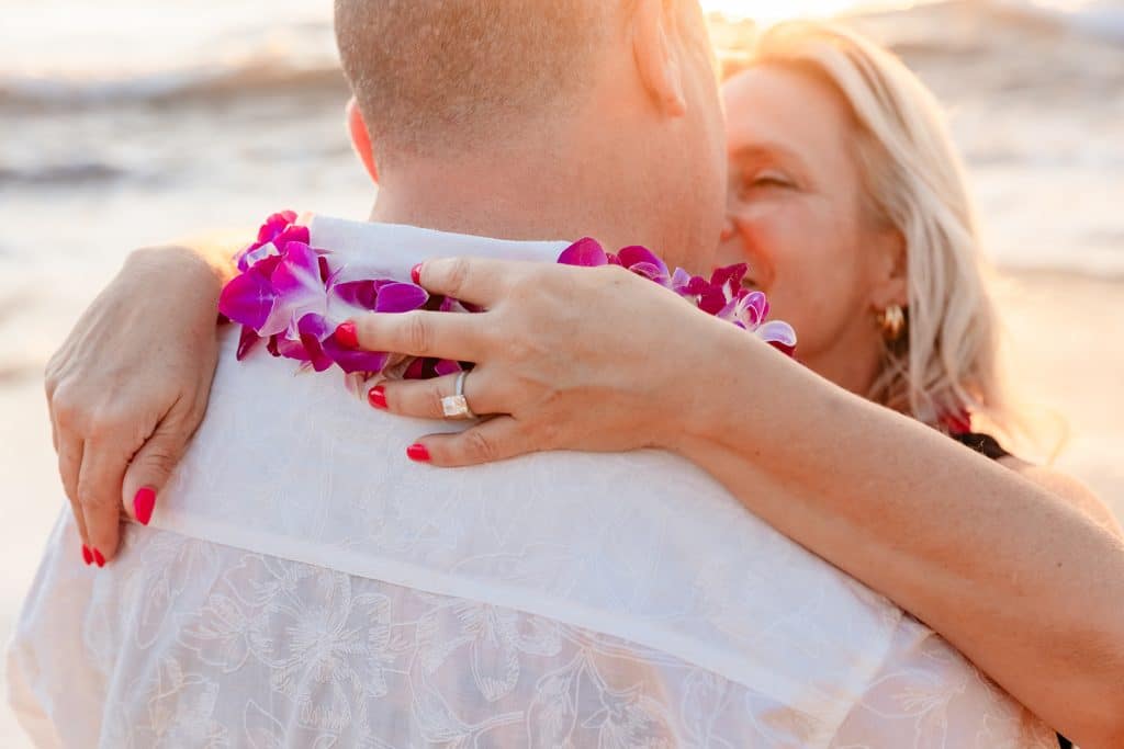 A close up photo of Joy's engagement ring as her hands are hugging Andy's neck and are placed on his lei.