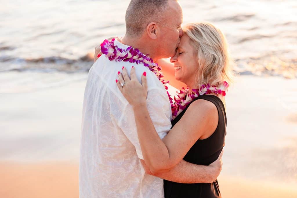 Andy holding Joy around the waist as she hugs his neck and giving her a kiss on the forehead next to the coast.
