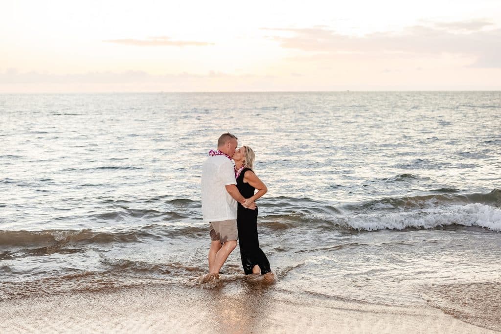 Andy and Joy standing in the ocean and sharing a kiss as the sun sets past the horizon of the water.