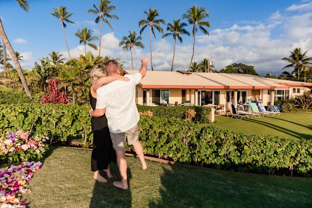 Joy hugging Andy as he holds Joy around her waist. They're facing a family who is outside cheering them on from a patio and Andy gives the aloha symbol to them