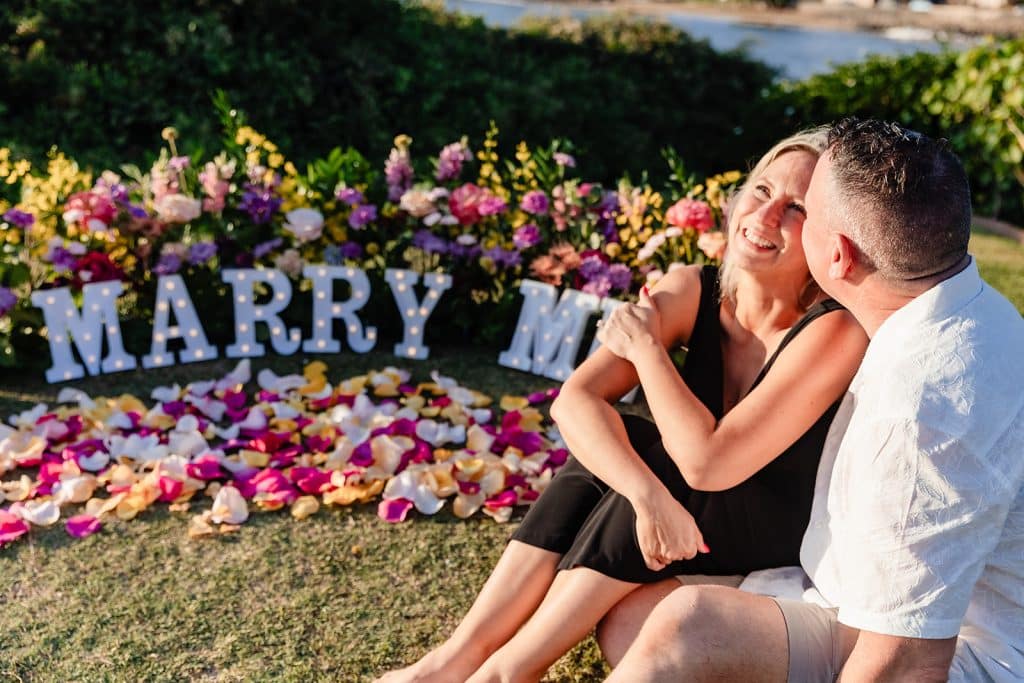 Andy and Joy sitting in front of the florals and marquee letters. Andy is giving Joy a kiss as she looks up and laughs.