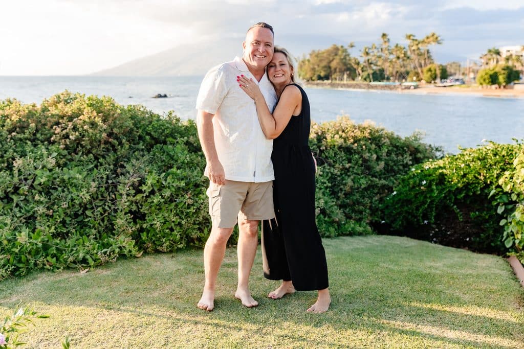 Andy and Joy smiling at the camera with the water behind them. Joy has her hand on Andy's chest as he holds onto her waist.