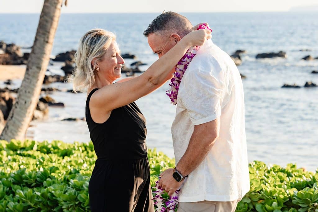 Joy placing a lei around Andy's neck as he leans into the placement. 