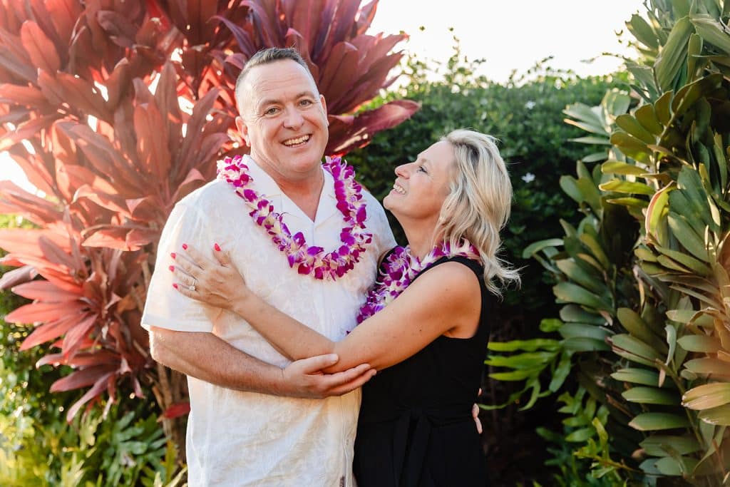 Andy and Joy standing in front of greenery as Andy smiles at the camera while Joy is smiling at him. They have their arms wrapped around each other.