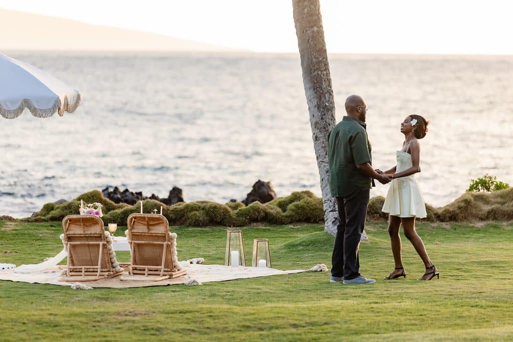 The man, Ernest, grabbing Gloria's hands next to the sunset picnic proposal blanket as he tells her that the romantic setup is for her.