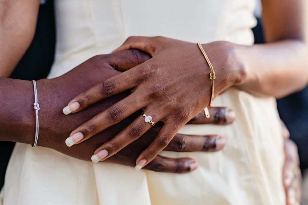 A close up photo of Gloria's hand with long nails and an oval solitaire engagement ring.
